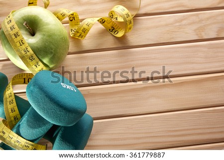 Green dumbbells, apple and tape measure on wooden floor. Concept health, diet and sports. Horizontal composition. Top view