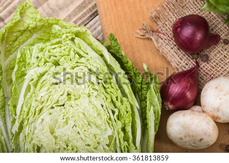 One half of fresh green white chinese cabbage with raw mushrooms purple onions on wooden board decorated with burlap and black pepper on table, horizontal picture