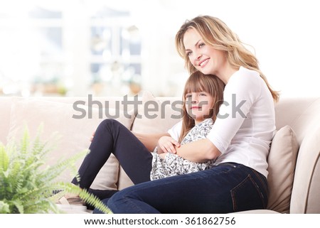 Portrait of happy mother embracing her cute daughter while sitting at living room at home. Happy family relaxing on the coach. 