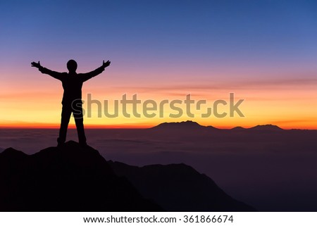 silhouette of man standing and spread hand on the top of mountain to enjoy colourful sky. Royalty-Free Stock Photo #361866674