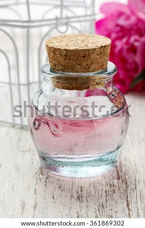 Bottle of pink essential oil and peony flower in the background