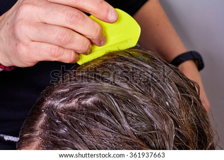 person checking wet hair for lice, with a yellow lice comb