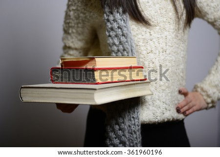 Eastern brunette girl holding education books, hipster in winter clothing, photo studio, portrait of a woman isolated on gray background