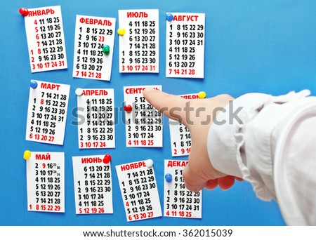 Hand pointing to the calendar for 2016, cut out and attached buttons on the wall. Focus on your finger.
