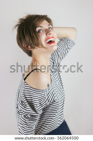 Colorful comic funny emotional woman laughing posing and having fun. Pretty girl laugh in stripped dress with fun hair, red lips, big smile and beautiful teeth. Studio photo on gray background.