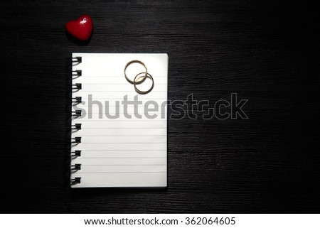 Blank notebook with heart and wedding rings on black background