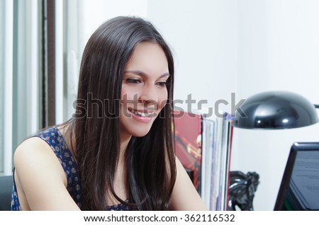 Hispanic brunette office woman sitting by desk and working on computer with positive attitude smiling