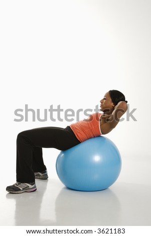Side view of African American woman balancing on exercise ball doing crunches.