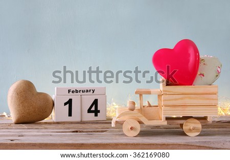 photo of February 14th wooden vintage calendar with wooden toy truck with hearts and gold garland. valentine's day celebration concept