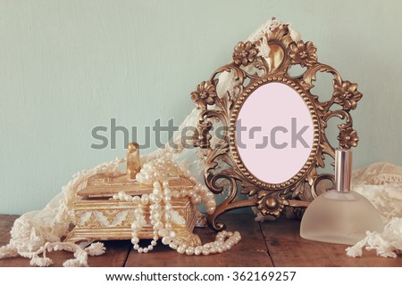 Antique blank victorian style frame, perfume bottle and white pearls on wooden table. template, ready to put photography
