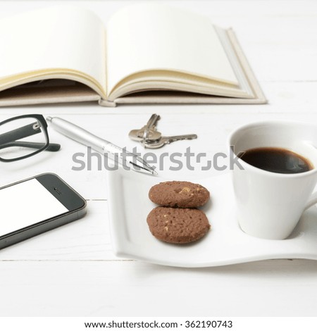 coffee cup with cookie,phone,open notebook and eyeglasses on white wood table