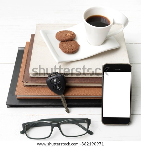 coffee cup with cookie,phone,stack of book and car key on white wood table