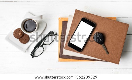 coffe cup with cookie,phone,car key,eyeglasses and stack of book on white wood table