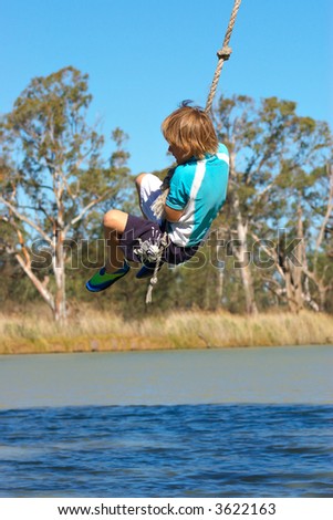 a boy is swinging on a rope over a river in summer