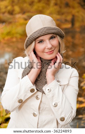 Picture of a young happy smiling blond girl in a hat standing in the autumn park near the lake