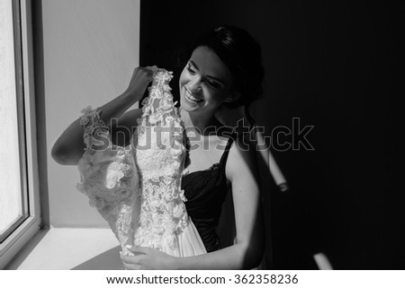 bride sitting on a windowsill and holds wedding dress