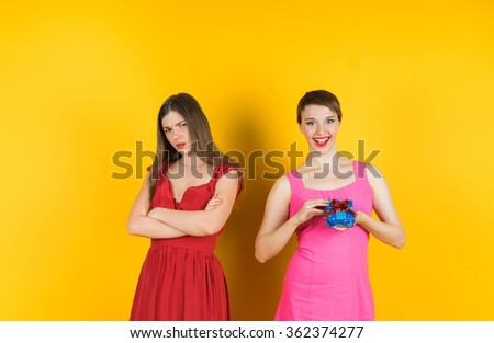 The girl received a gift, and the other girl looks with angry. Isolated studio  yellow background female model. Royalty-Free Stock Photo #362374277