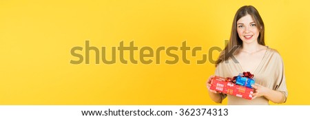 Portrait of casual young happy smiling woman hold 2 gift boxes. Isolated studio  yellow background female model. wide banner.