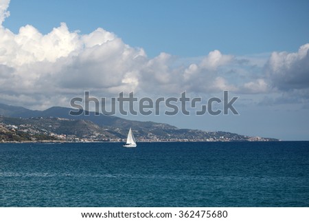 Photo of beautiful white sailing boat in blue sea seaside mountains silhouetted against milky cloudy sky and seascape background, horizontal picture