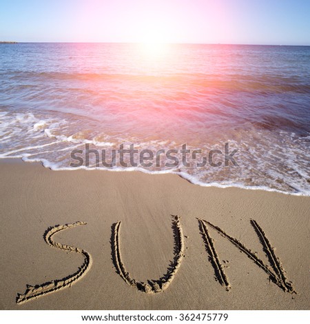 Photo closeup with sun spot of word sun written on wet beige beach sea marine grained sand against blue waves with white spindrifts running on seashore on seascape background, square picture
