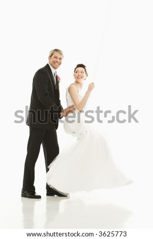 Portrait of Caucasian groom pushing Asian bride in swing.