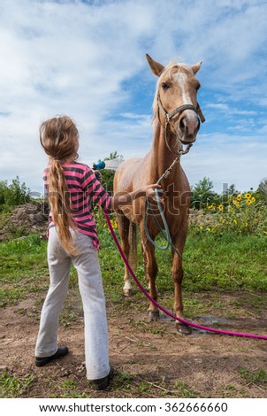 Girl washing a horse with a hose on a farm Royalty-Free Stock Photo #362666660