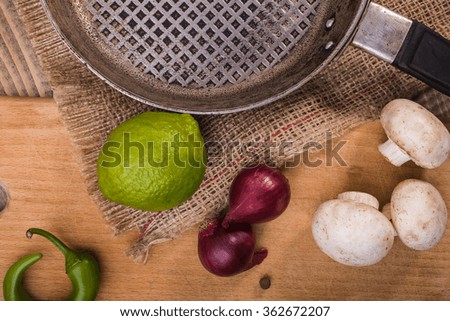 Juicy crude lime near frying pan on burlap with champignons purple onions and green chili pepper on cutting plank on table, horizontal picture