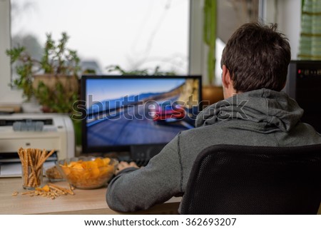 male gamer playing racing game on computer with snacks lying on table - stock photo