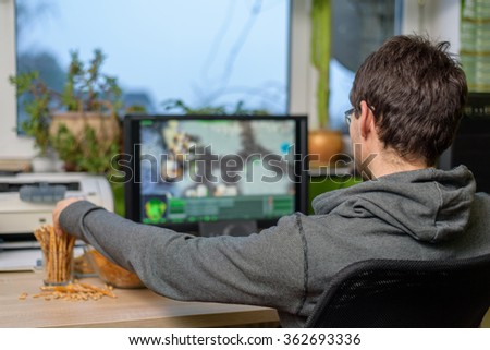 male gamer playing strategy game on computer with snacks lying on table - stock photo