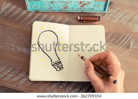Retro effect and toned image of a woman hand drawing a light bulb with a fountain pen on a notebook. Copy space available, ideas creativity conceptual image