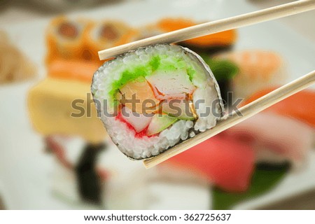 Sushi in chopsticks with blur sushi on a plate background