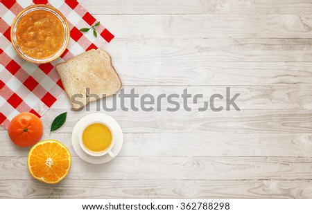 Fruit breakfast with free space on table. Jar of jam, orange, tangerine,
raspberries, tea, toast.