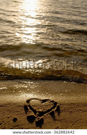 Lovely small heart drawn in salt  sand at beach. Evening warm colors of sun mirror in water level.
