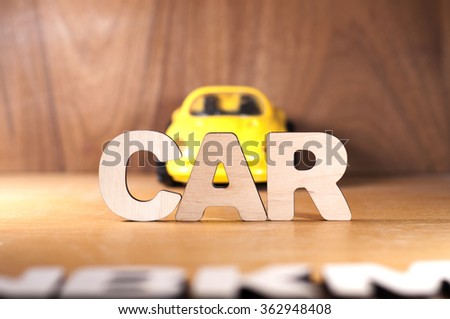 The word CAR made of wooden letter, with a yellow toy car in the background.
