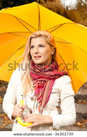 Picture of a young elegant woman in a casual clothes and an orange scarf under the yellow umbrella in autumn forest