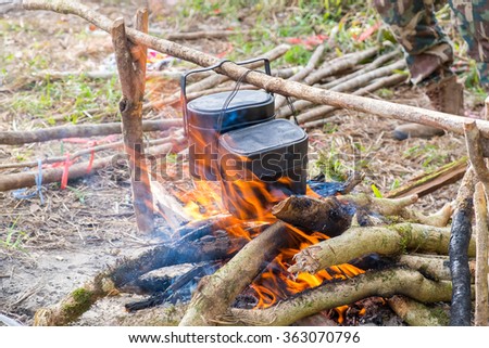 Rice cooking with army pot on bonfire with orange flames and firewood
