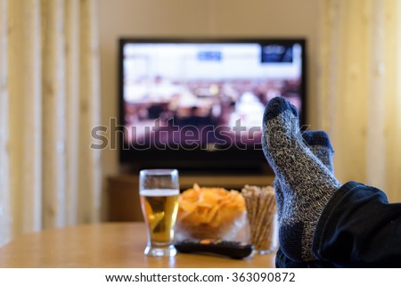 TV, television watching (tank on street, war movie) with feet on the table and snacks - stock photo