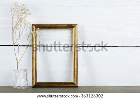 Golden wooden photo frame with dried flowers in a jar on wooden background