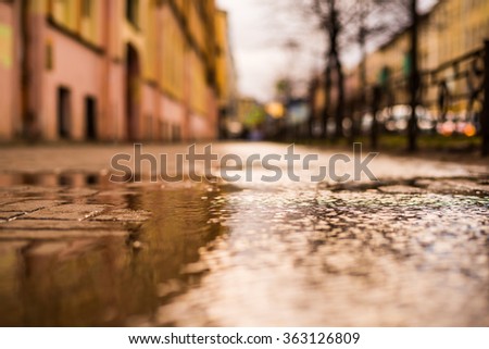 Streets in the late autumn after rain, empty street. View from the level of the puddle on the sidewalk