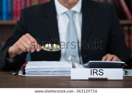 Midsection of tax auditor examining documents with magnifying glass at table in office Royalty-Free Stock Photo #363129716