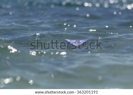 Photo closeup of one white paper origami boat riding on blue salt sea waves ocean water surface with ripples on blurred bokeh seascape background, horizontal picture 