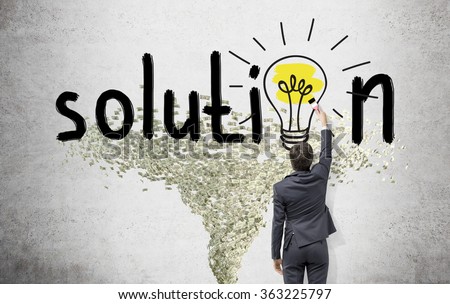 Young businessman painting a bright yellow bulb with a brush in the word 'solution' instead of the second 'o' on the white wall. Dollar tornado under it. Back view. Concept of finding a solution.