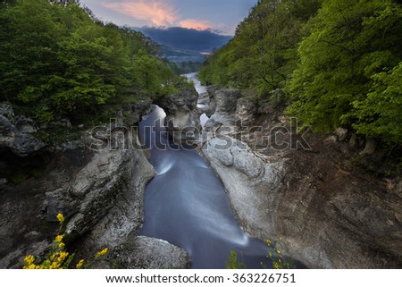 The mountain river in the gorge. Water on the long exposure. Landscape of the river between the rocks. Water flow. Green trees in the gorge. Beautiful view of rocks and river.