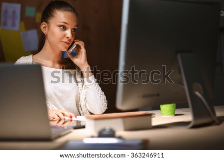 Young woman working in office, sitting at desk and talk on the phone