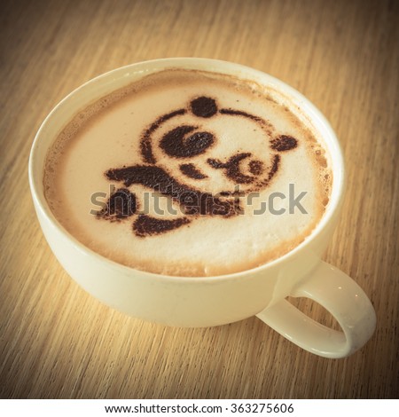 Top view of a giant panda (or panda bear) shape foam art of a cappuccino cup with saucer on wooden table background in the natural light of afternoon. Panda latte art drawing cafe cup in vintage style