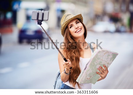 young female tourist with map taking selfie on city street