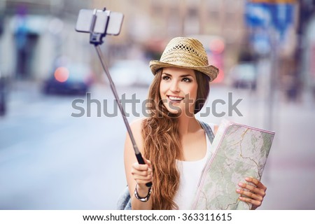 Happy young female tourist with map taking selfie on city street