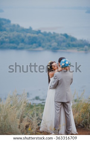 Beautiful young wedding couple is kissing on the top of the hill at natural summer background.