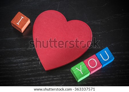 Love concept. Valentines day background with red heart and I Love You message written in wooden blocks. Cross processed image with selective focus