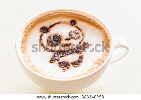 Top view of a giant panda (or panda bear) shape foam art of a cappuccino cup with saucer on wooden table background in the natural light of afternoon. Latte art drawing coffee cup with cute panda face